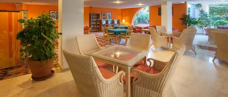 A hotel lobby with wicker furniture, a glass-top table, a potted plant, and a bookshelf.