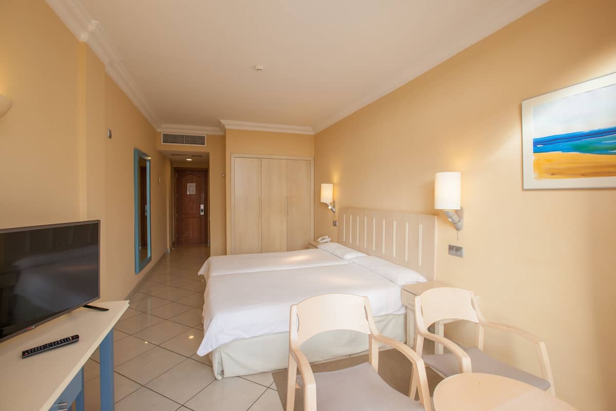 A hotel room with two beds, a TV, a desk, and a chair.