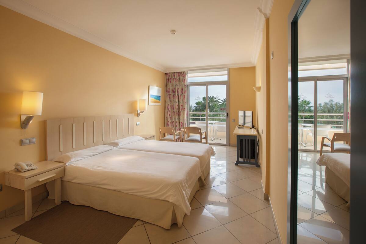 A hotel room with two beds, a balcony, and a view of the outdoors.
