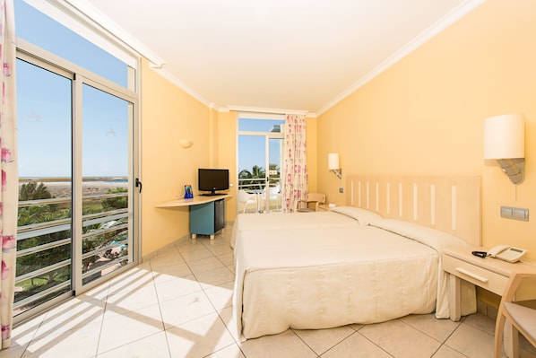 Habitación de hotel con cama, escritorio con televisor, teléfono y vista al exterior.