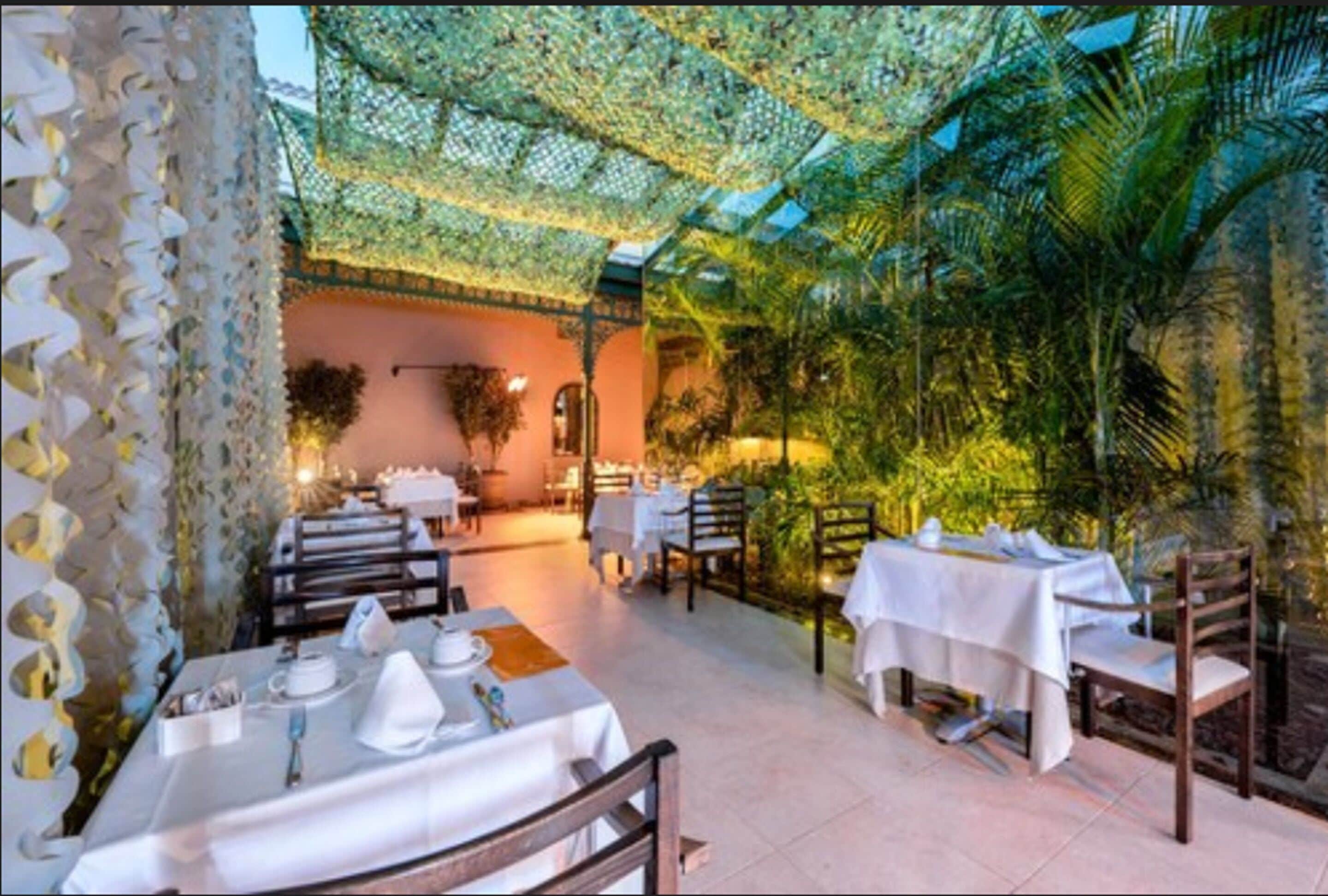 Un espace de restauration intérieur avec des tables dressées, un mur décoré de motifs et un décor de plantes tropicales en arrière-plan.
