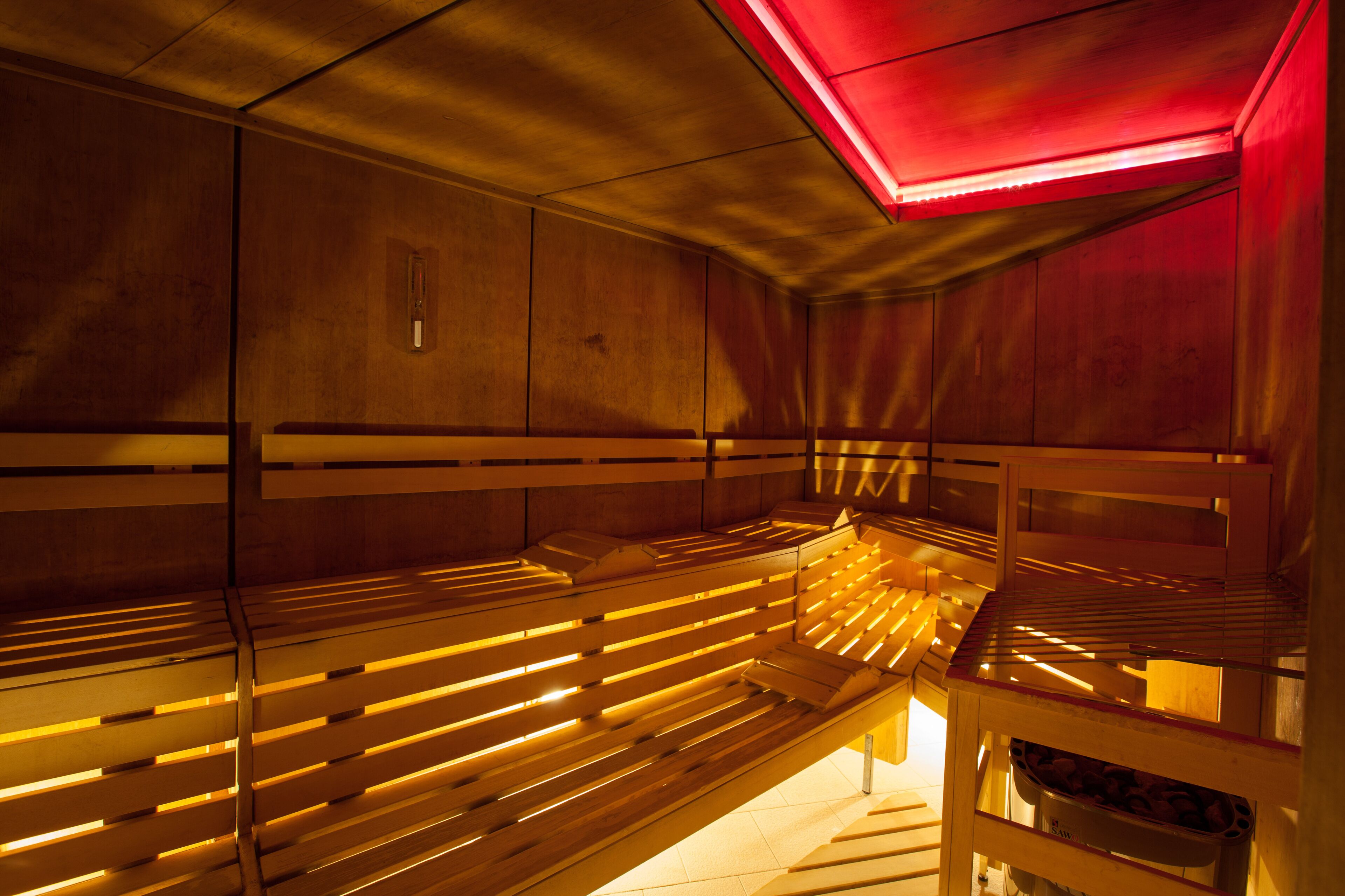 Sala de sauna com bancos de madeira e luminária vermelha.