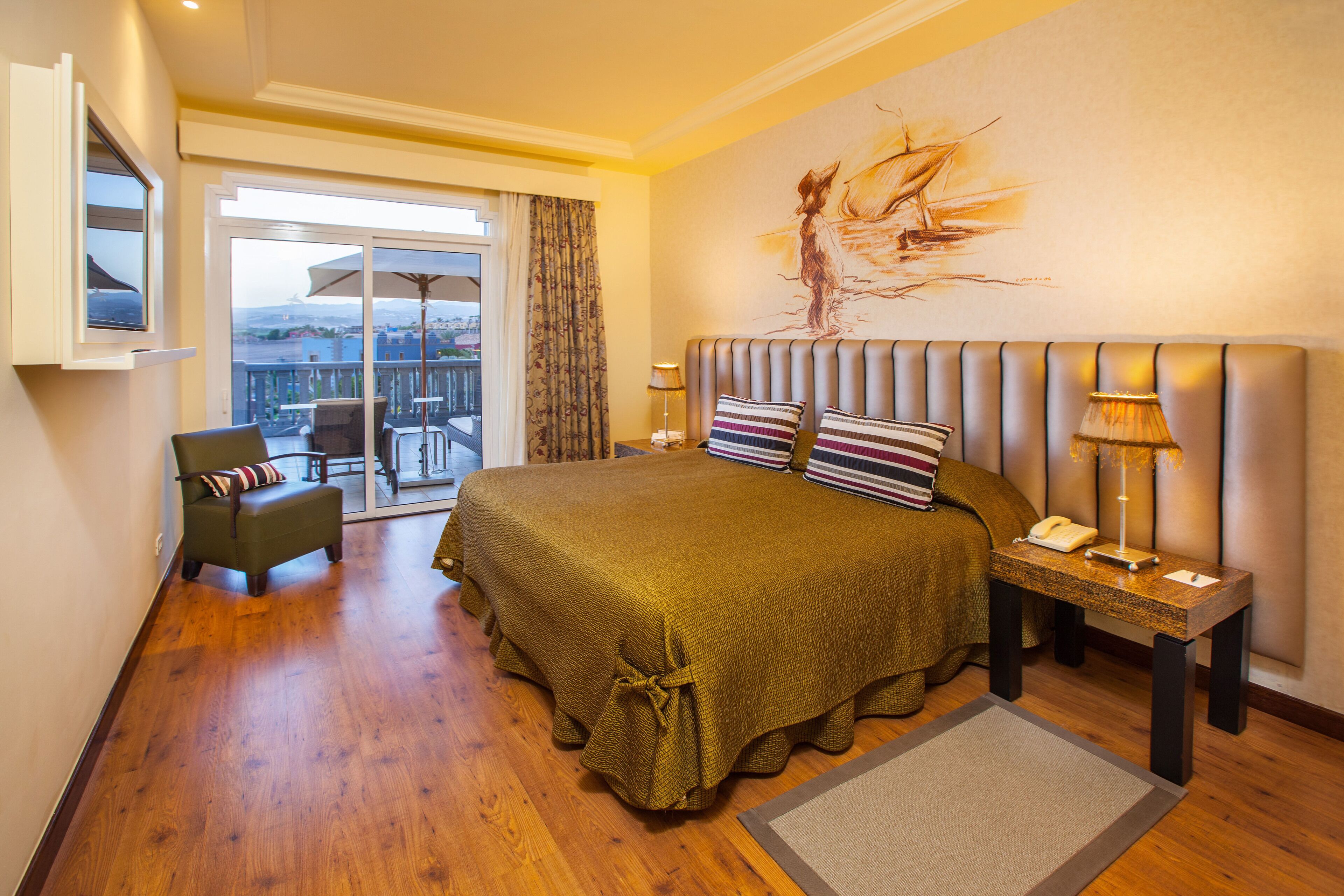 Habitación de hotel con una cama grande, una silla, una mesita de noche y vistas a la ciudad desde un balcón.