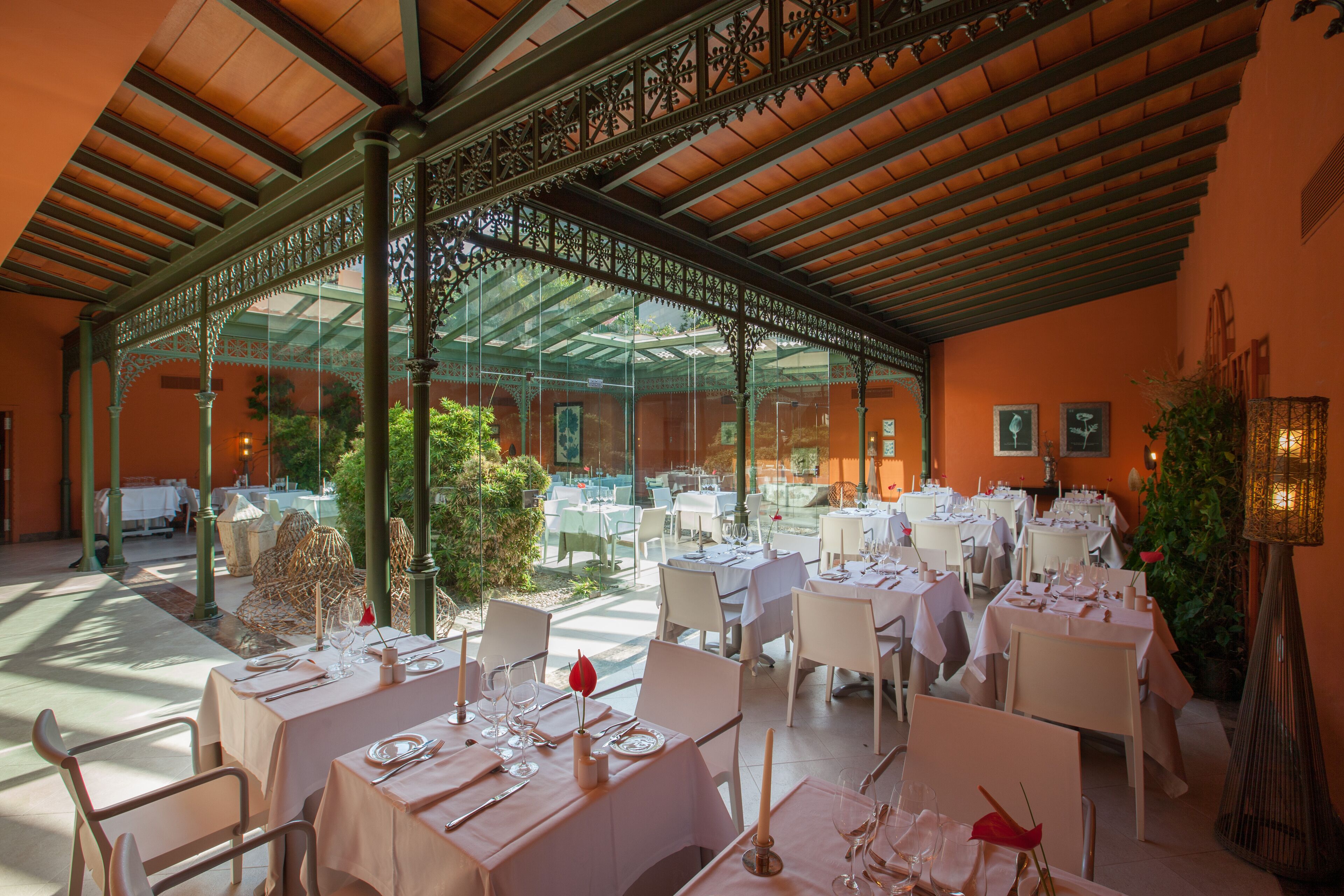 Ein Restaurant mit Außenbereich, überdacht durch eine Stahl- und Glaskonstruktion, mit gedeckten Tischen.