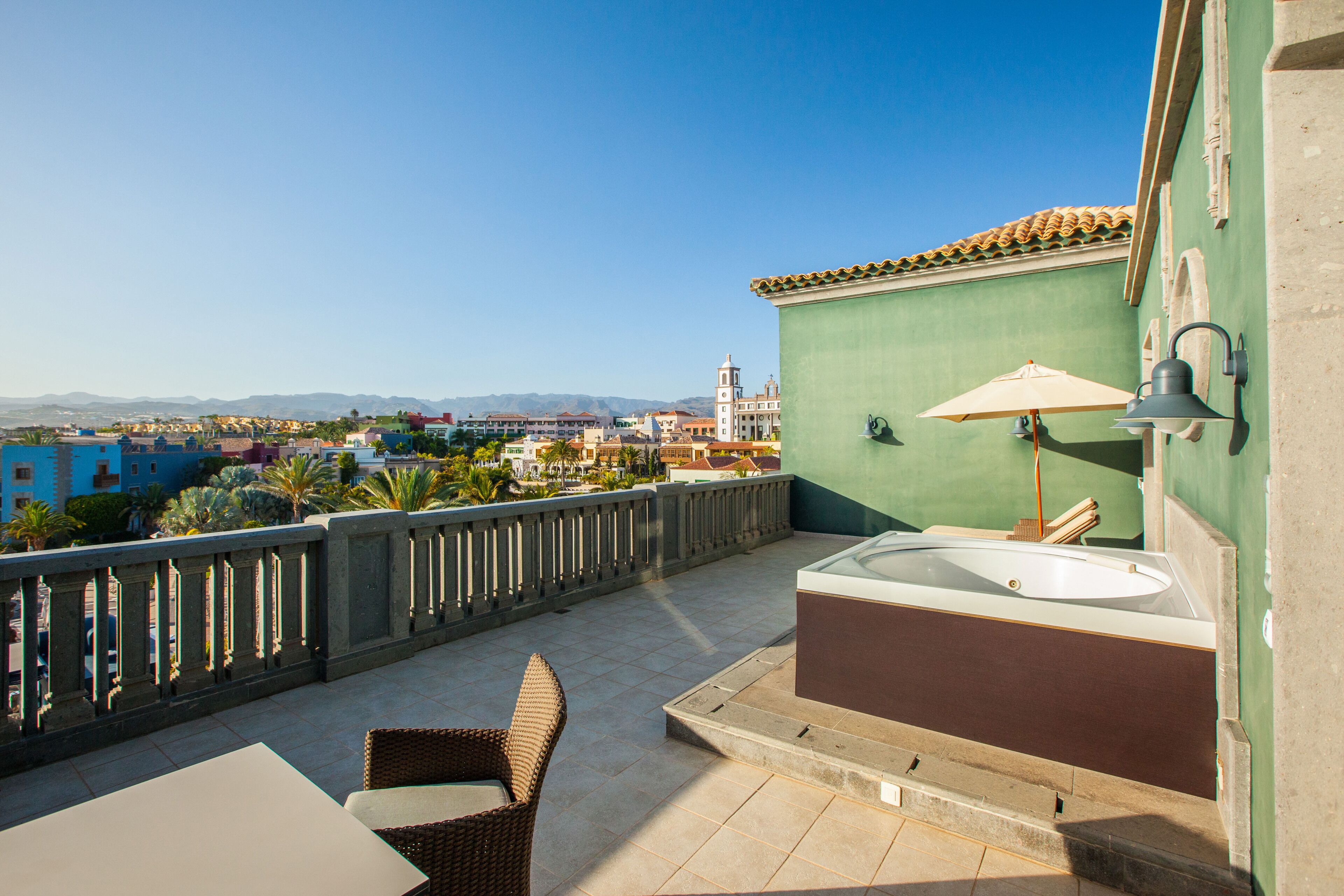 A balcony with a view of a cityscape, a bathtub, and wicker furniture.