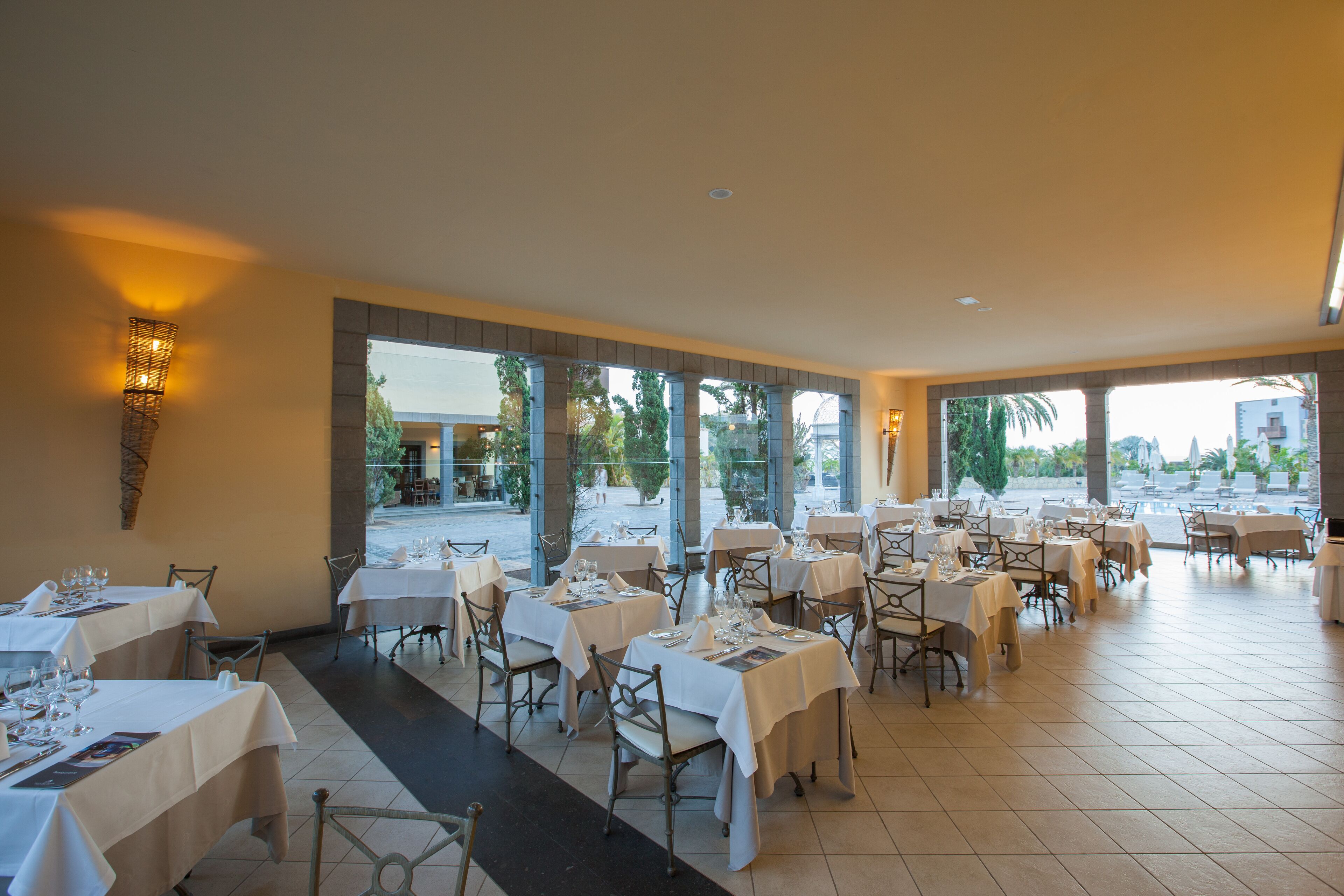 Un restaurante con varias mesas dispuestas para comer, ventanas amplias y vistas al exterior.