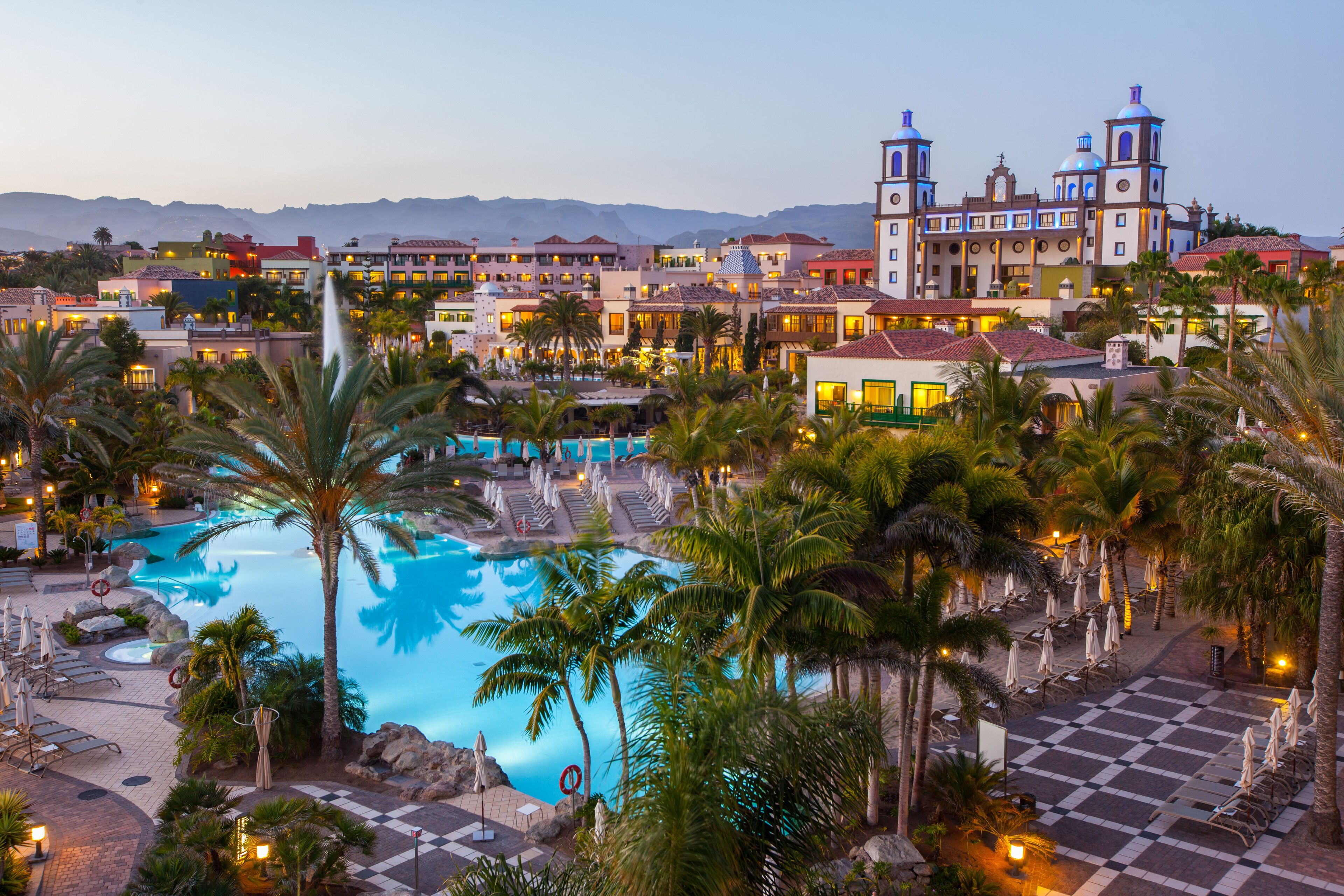 A resort with a large pool, palm trees, and a building with two towers.