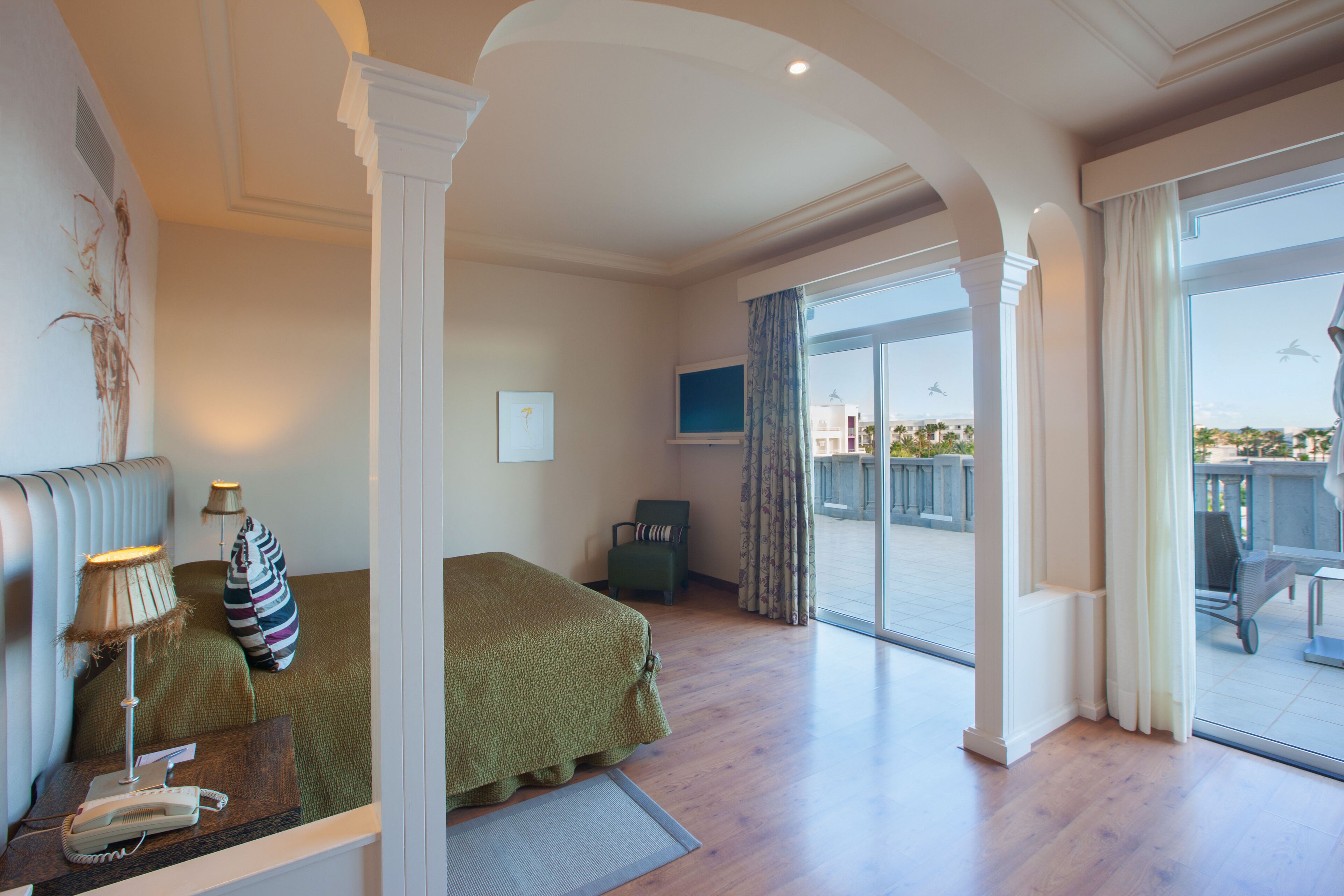 Habitación de hotel con cama, escritorio con lámpara, silla y vistas al exterior.