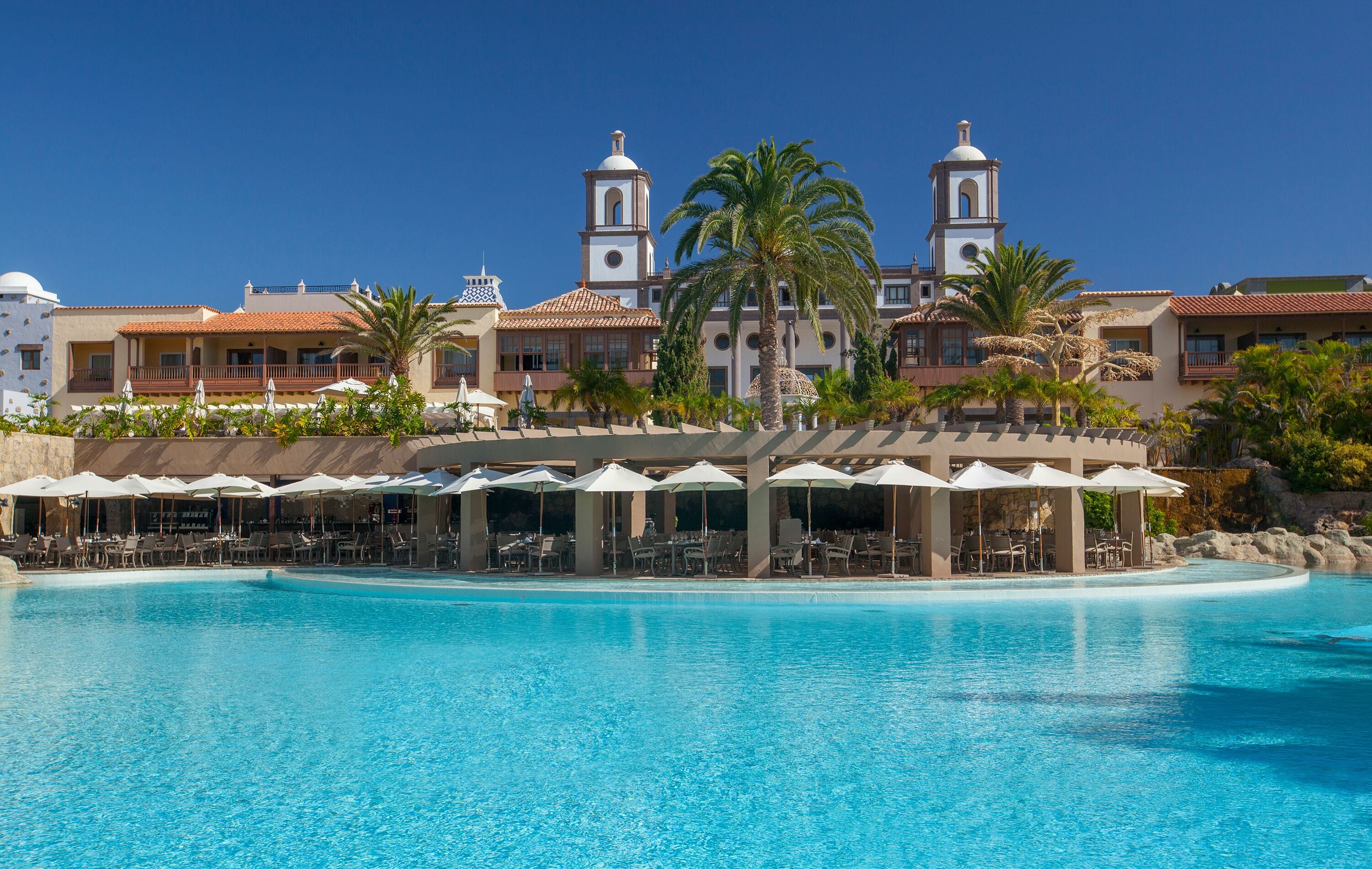 A resort with a large pool, outdoor seating, and a building with two towers.