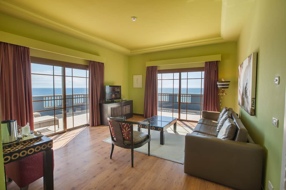 A living room with a sofa, a coffee table, a TV, and a view of the sea through large windows.
