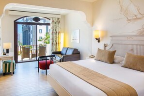 Une chambre d’hôtel avec un grand lit, un bureau, une chaise, un balcon avec des fauteuils et une vue sur les immebles.
