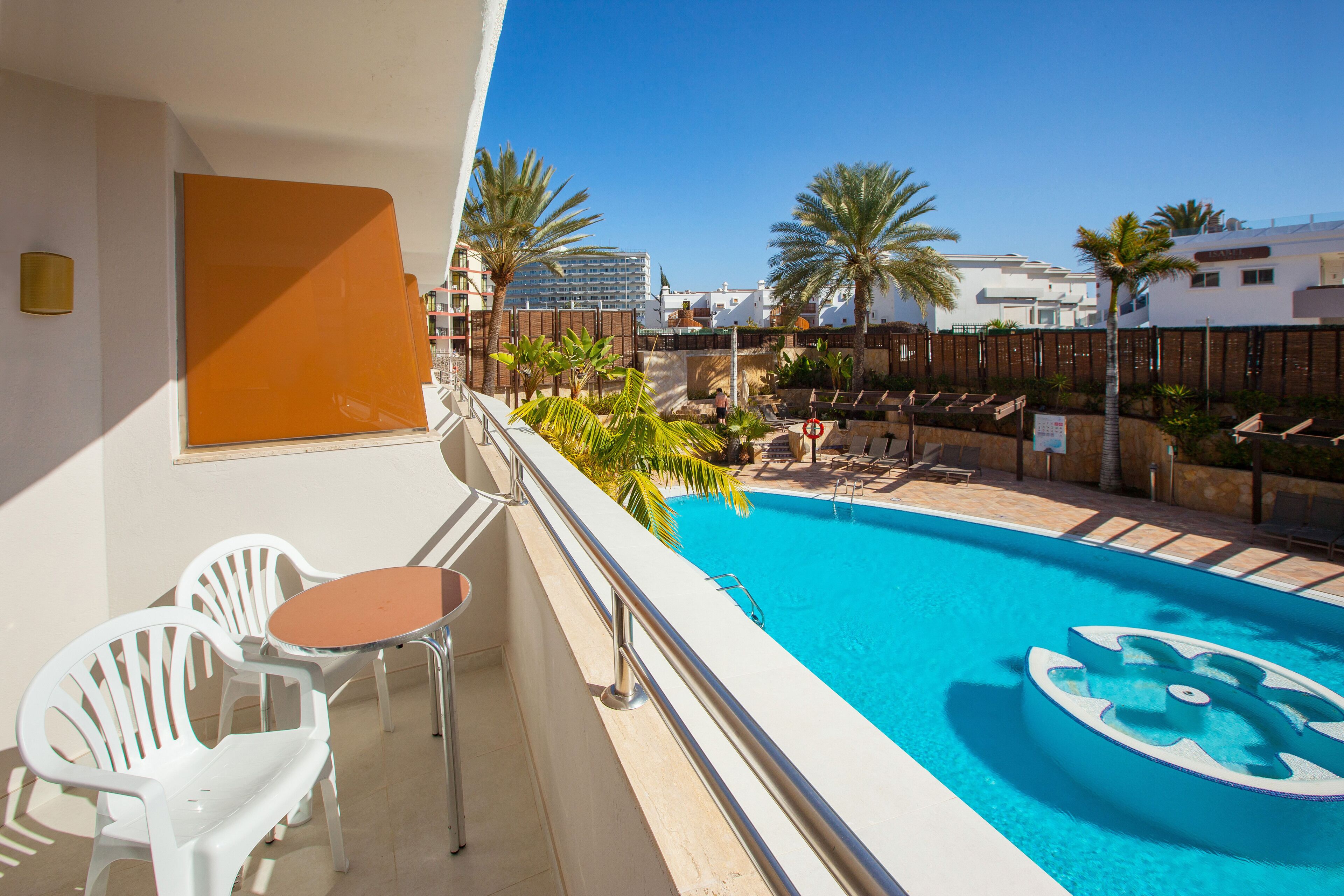 A balcony with a pool, white chairs, and a table.