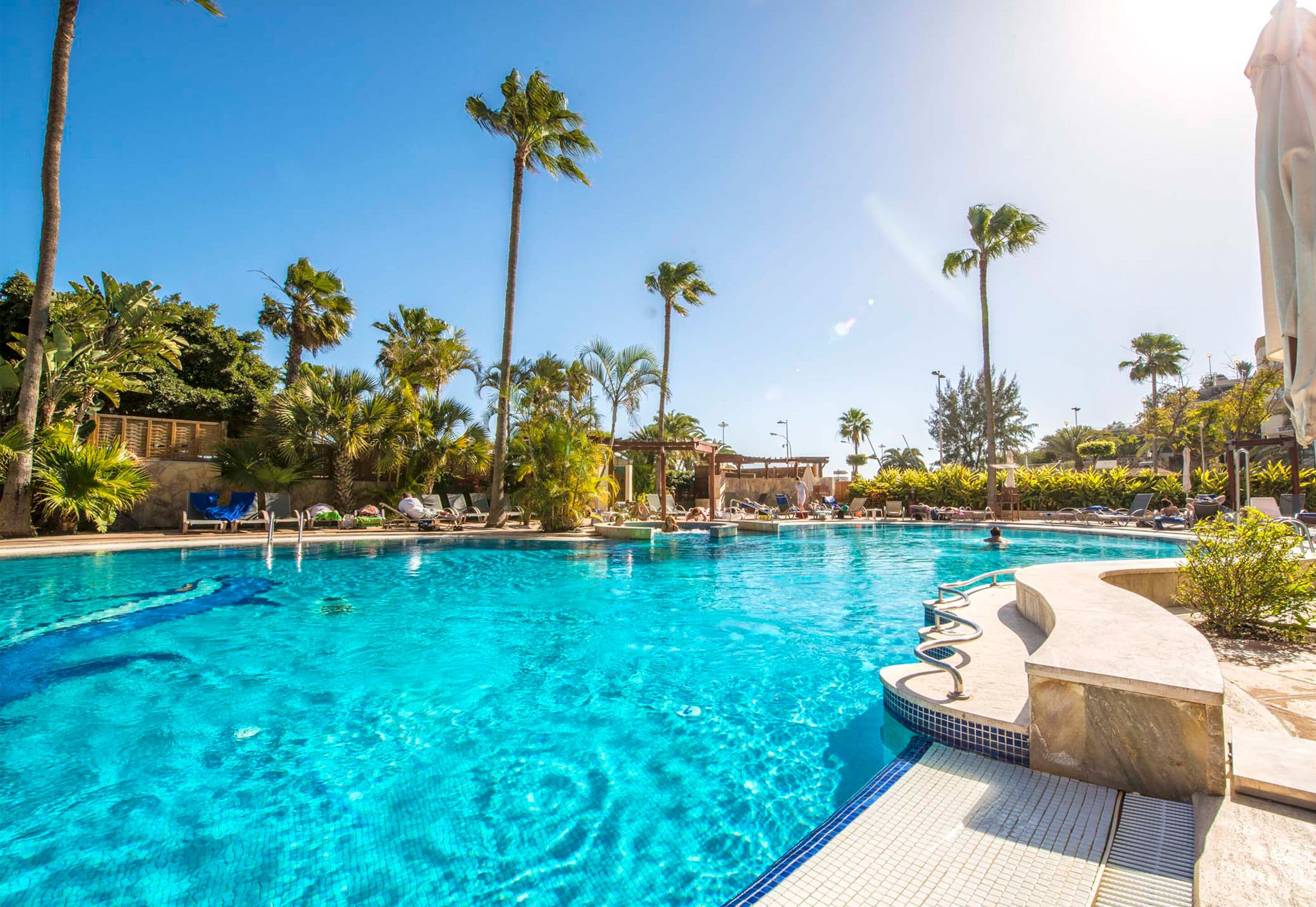 A clear blue pool surrounded by palm trees and lounge chairs.