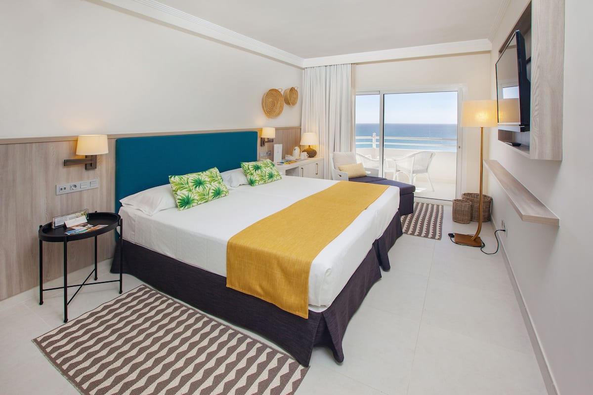 A hotel room with a large bed, a desk, a chair, a TV, and a view of the ocean.