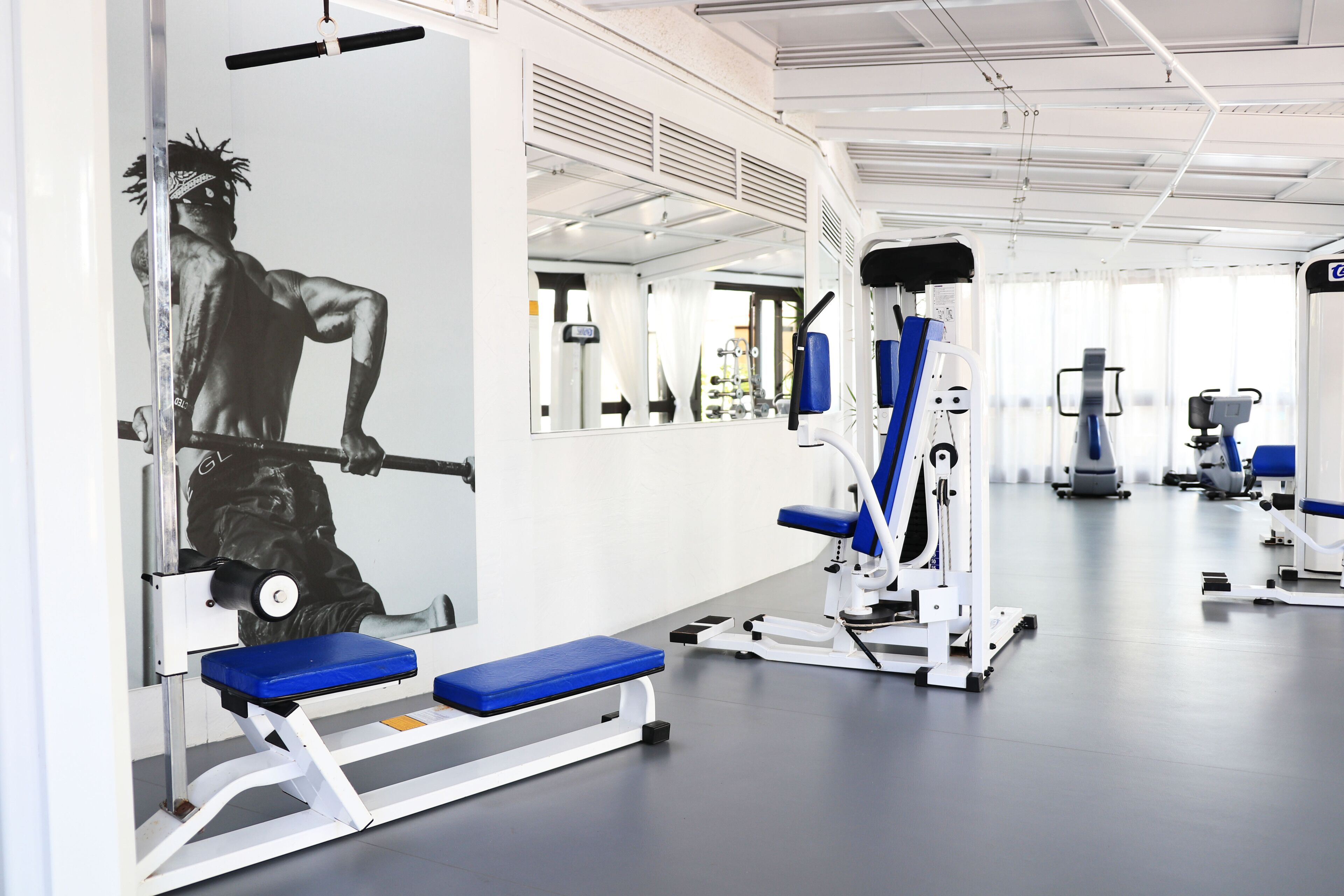 Un gimnasio con equipo de ejercicio, espejos y un banco azul.