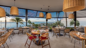 A restaurant with wicker pendant lights, wooden tables, and red cushioned chairs. - Corallium Dunamar by Lopesan Hotels - Adults Only (San Bartolomé de Tirajana)
