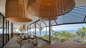 A modern lounge area with wicker ceiling lamps, a sofa set, and a view of the ocean. - Corallium Dunamar by Lopesan Hotels - Adults Only (San Bartolomé de Tirajana)