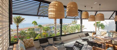 Un salón moderno con vista a la playa, que cuenta con lámparas colgantes de mimbre, un sofá y una mesa de centro.
