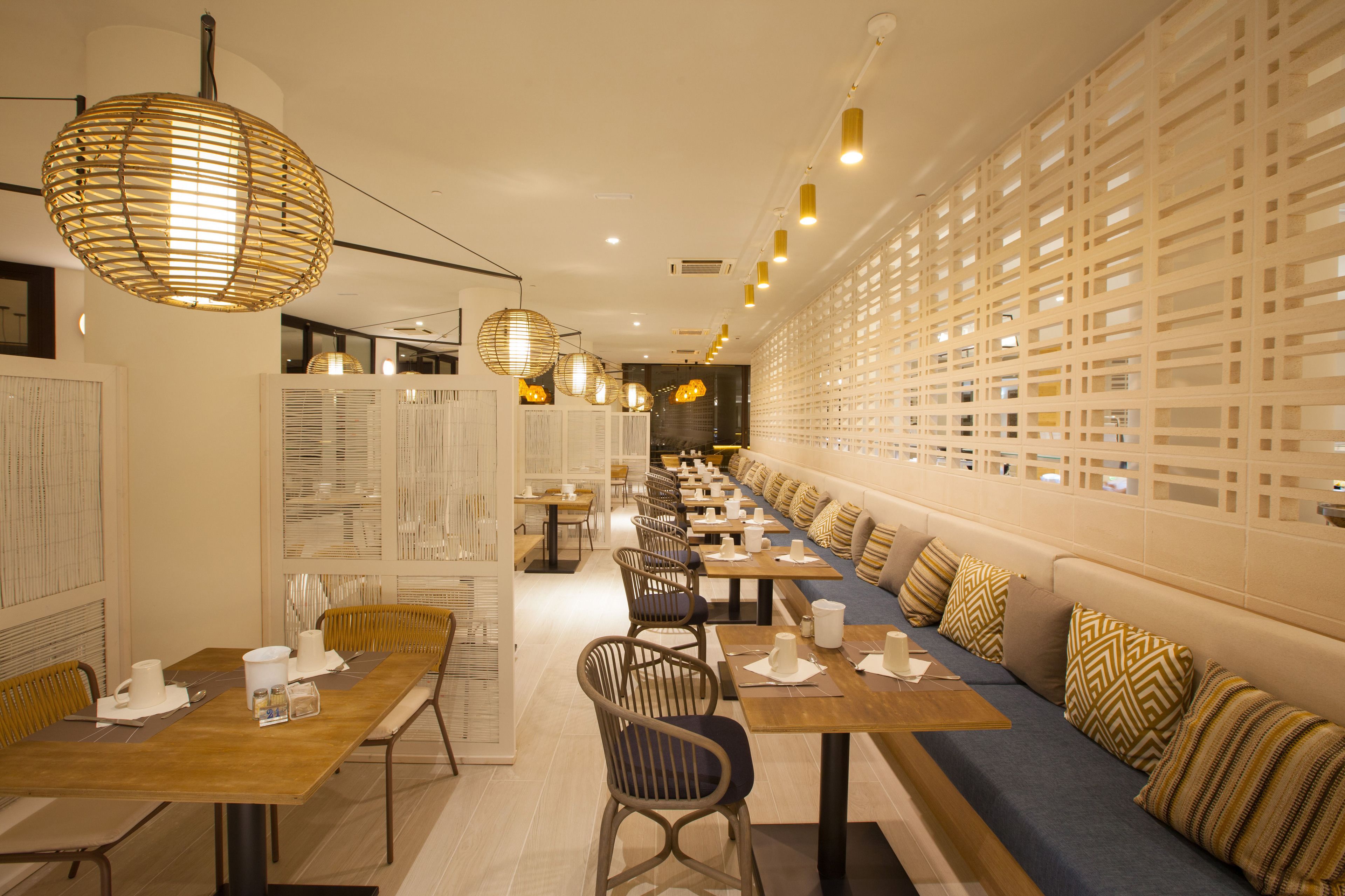 A modern restaurant with long communal tables, cushioned seating, and decorative lighting.