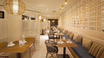 Un restaurante moderno con mesas comunitarias largas, asientos acolchados e iluminación decorativa.