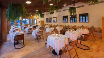 A restaurant with round tables and chairs, white tablecloths, and hanging plants.