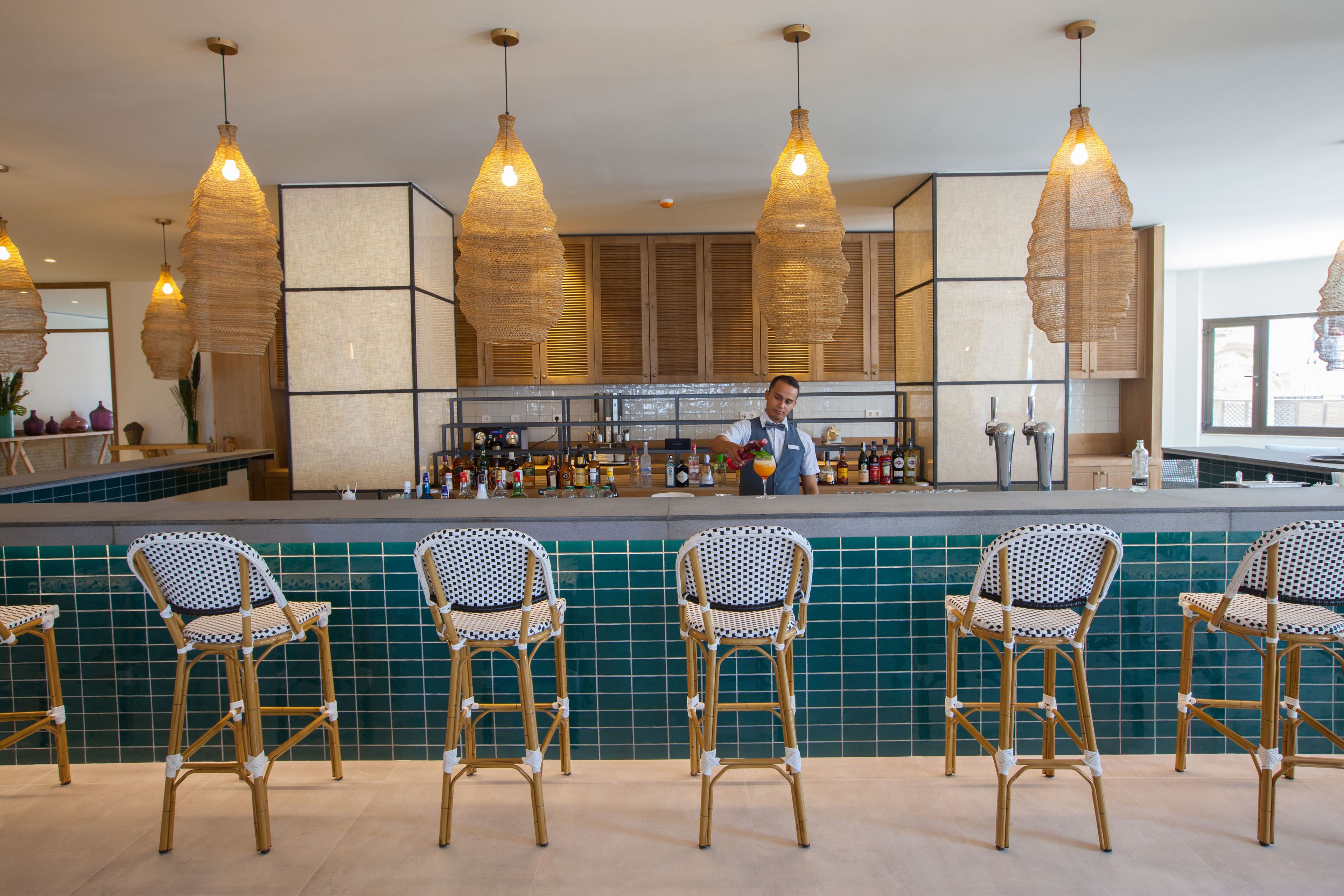 A bar area with wicker chairs, a bartender, and a tiled backsplash.