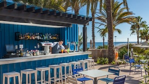 A bar area with a bartender, outdoor seating, and a view of the ocean. - Corallium Dunamar by Lopesan Hotels - Adults Only (San Bartolomé de Tirajana)