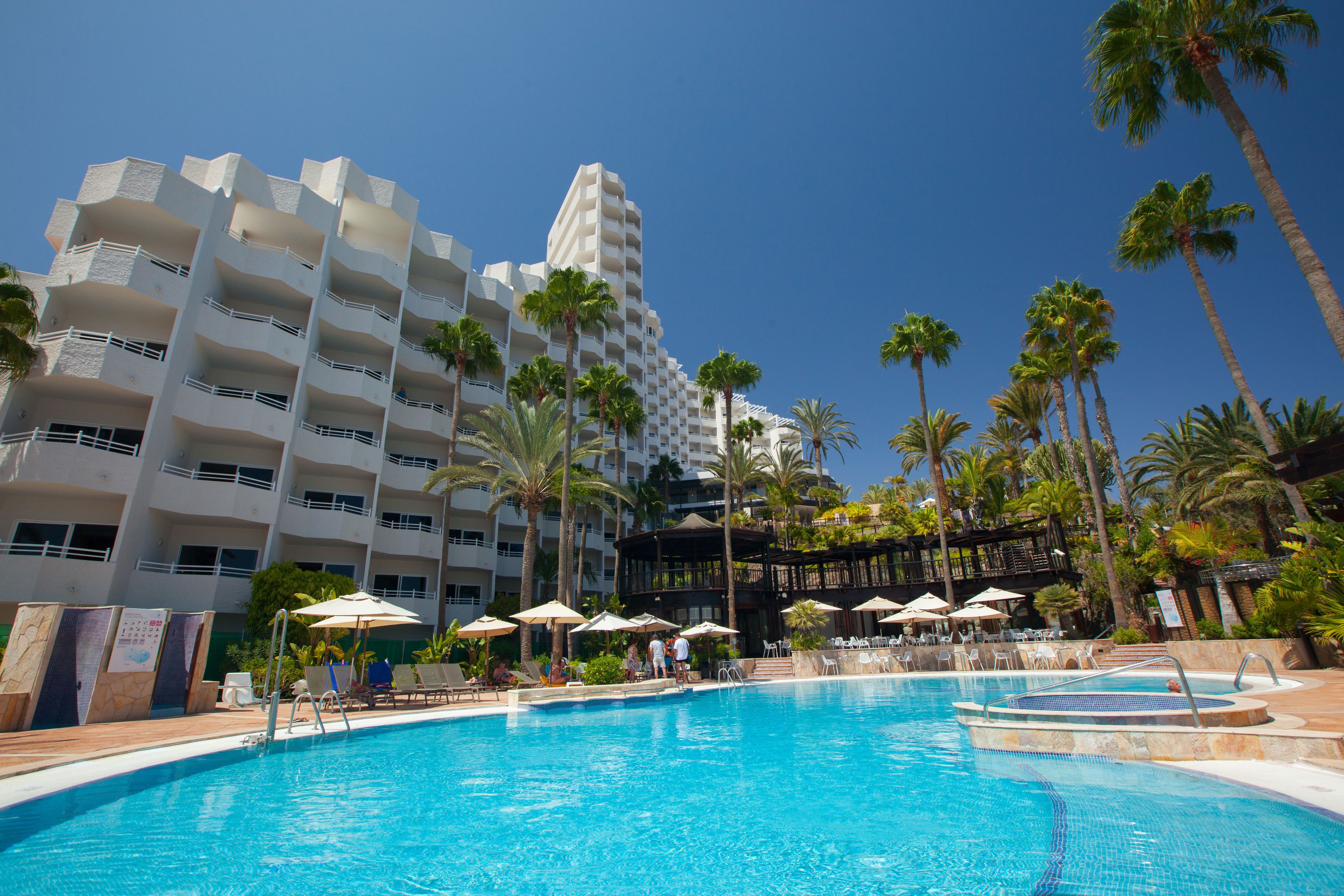 A hotel with a swimming pool, palm trees, and outdoor seating areas.