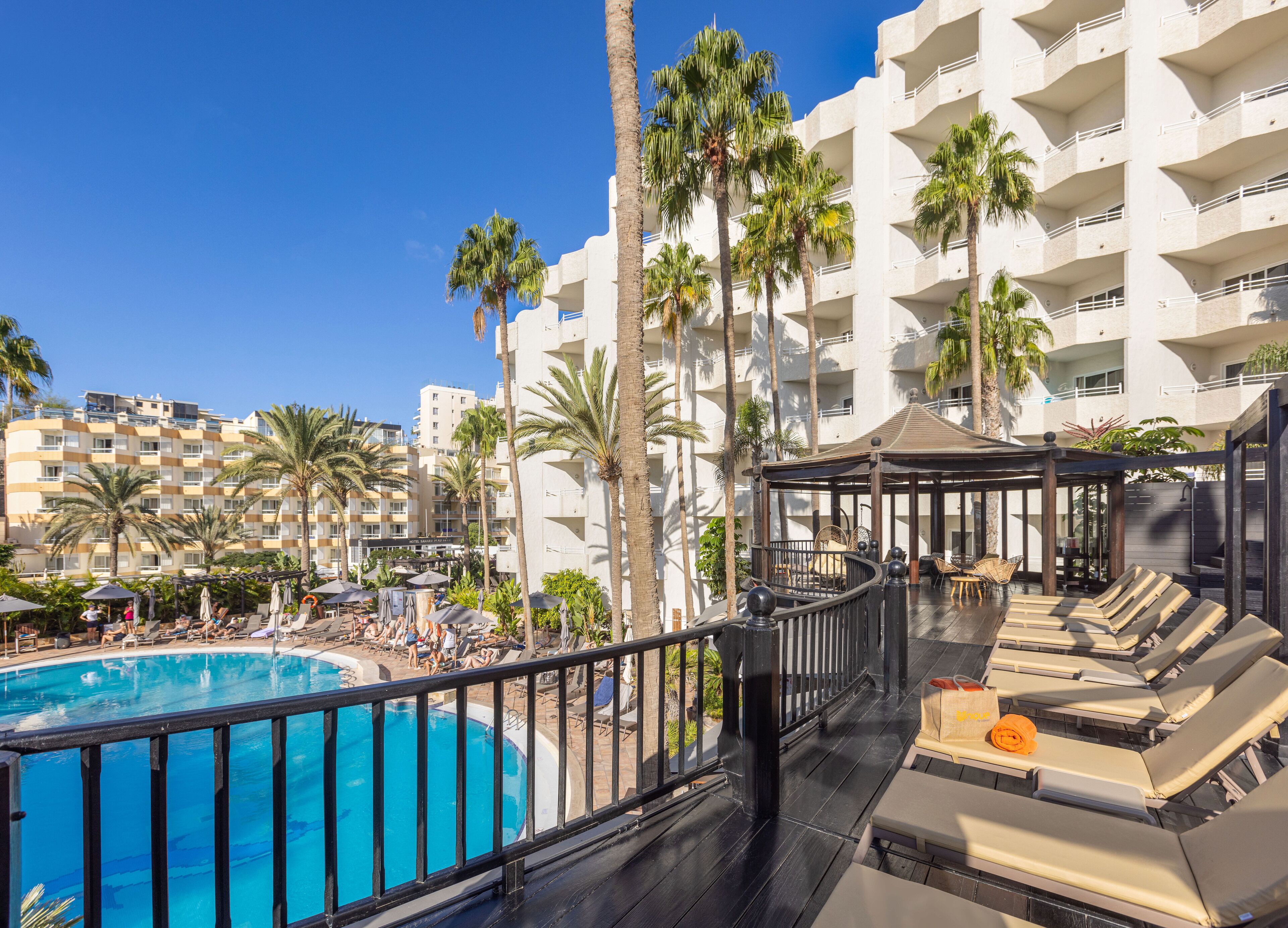 A resort pool area with lounge chairs, a cabana, and a view of the surrounding buildings.