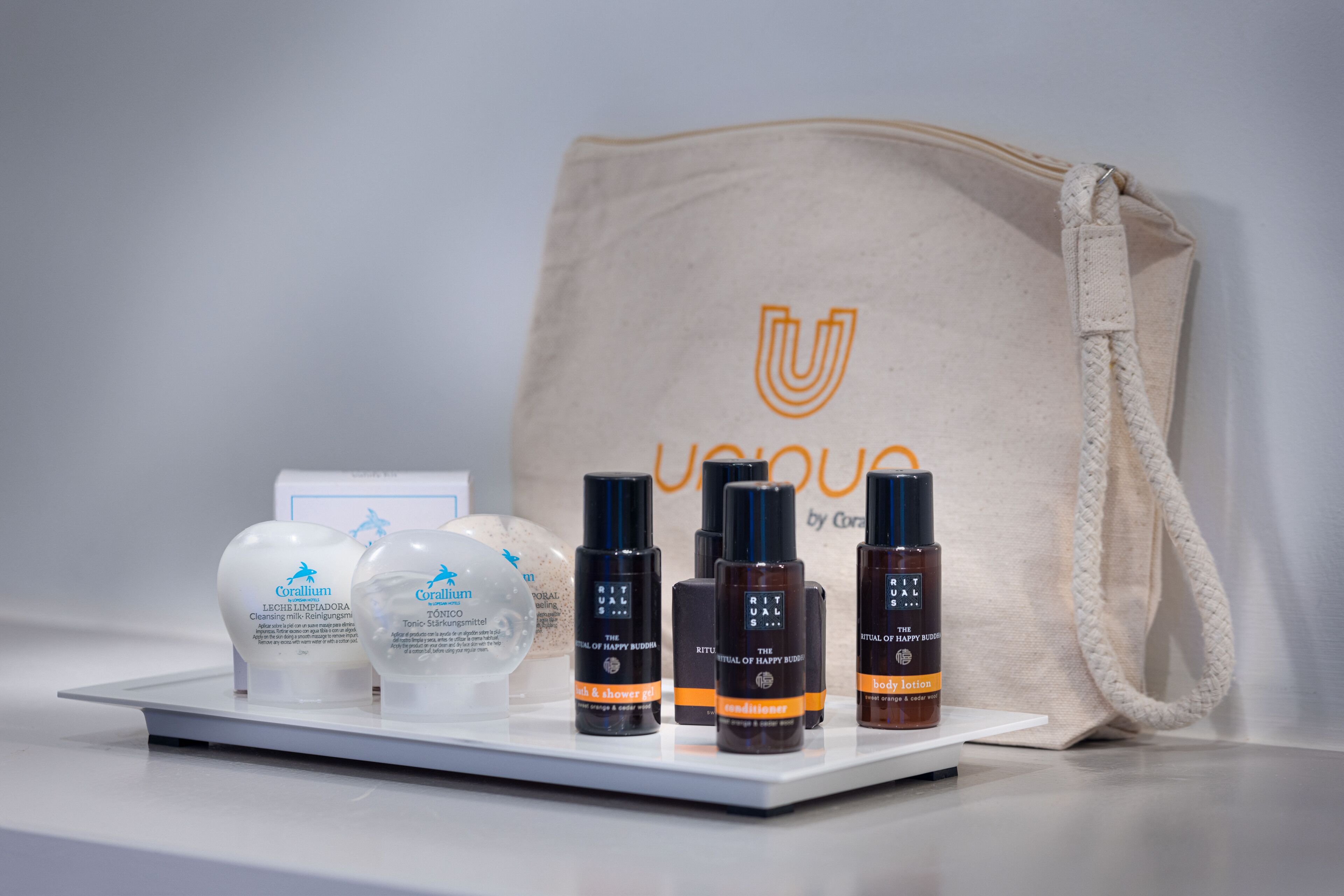 A display of Corailium body care products including lotion, shower gel, and body lotion, with a beige tote bag in the background.
