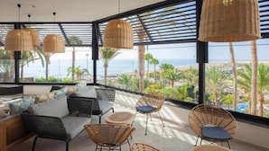 A modern lounge area with wicker furniture, large windows offering a view of the beach and ocean. - Corallium Dunamar by Lopesan Hotels - Adults Only (San Bartolomé de Tirajana)