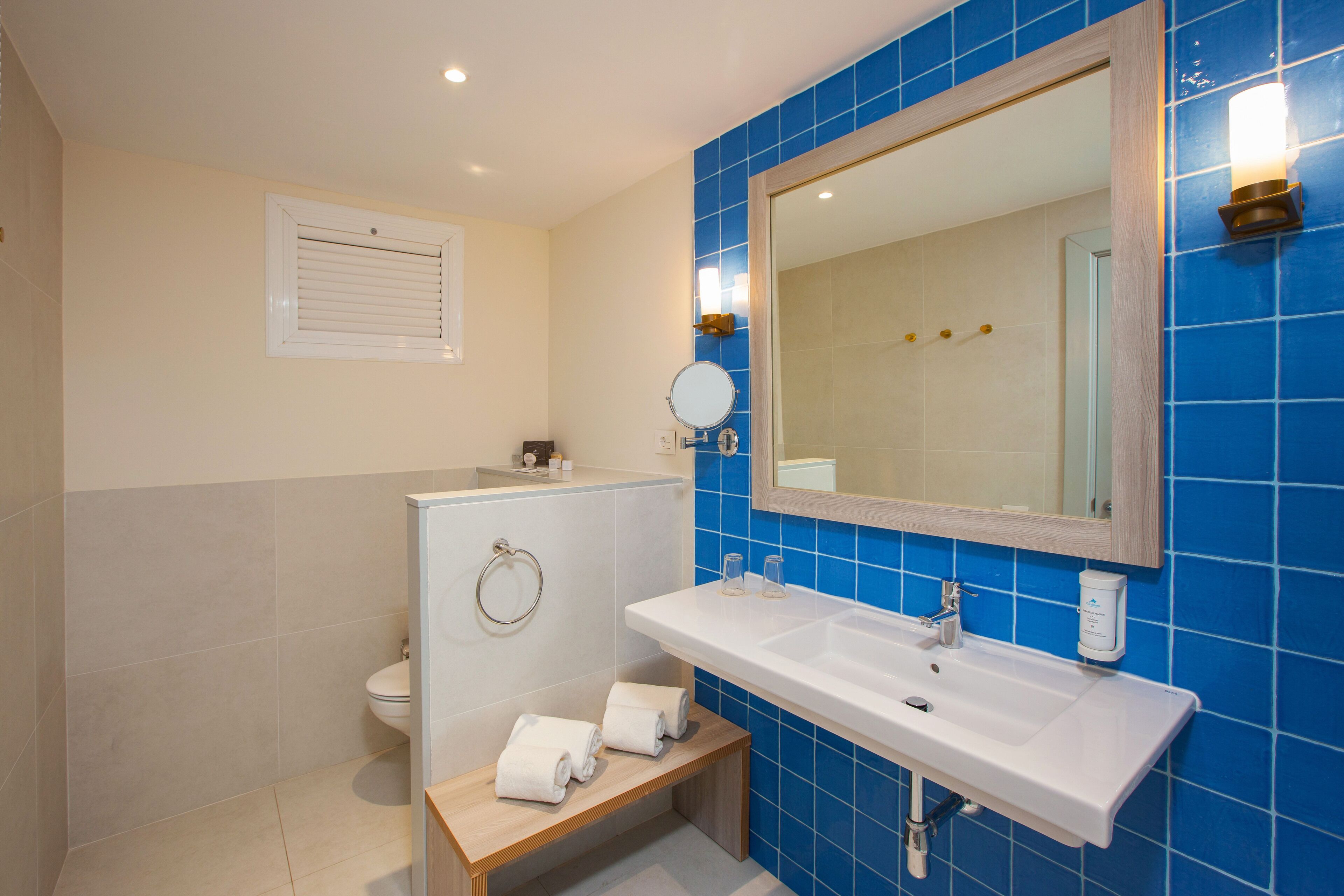 Un bagno con un lavandino bianco, piastrelle blu, uno specchio e un water.
