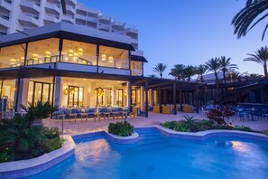 A modern hotel with a pool area, outdoor seating, and a well-lit lobby.
