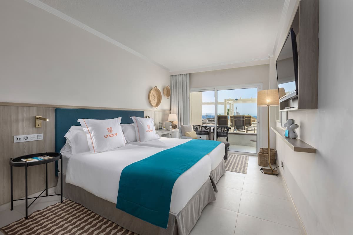 A hotel room with a large bed, a desk, a chair, a TV, and a balcony with a view.