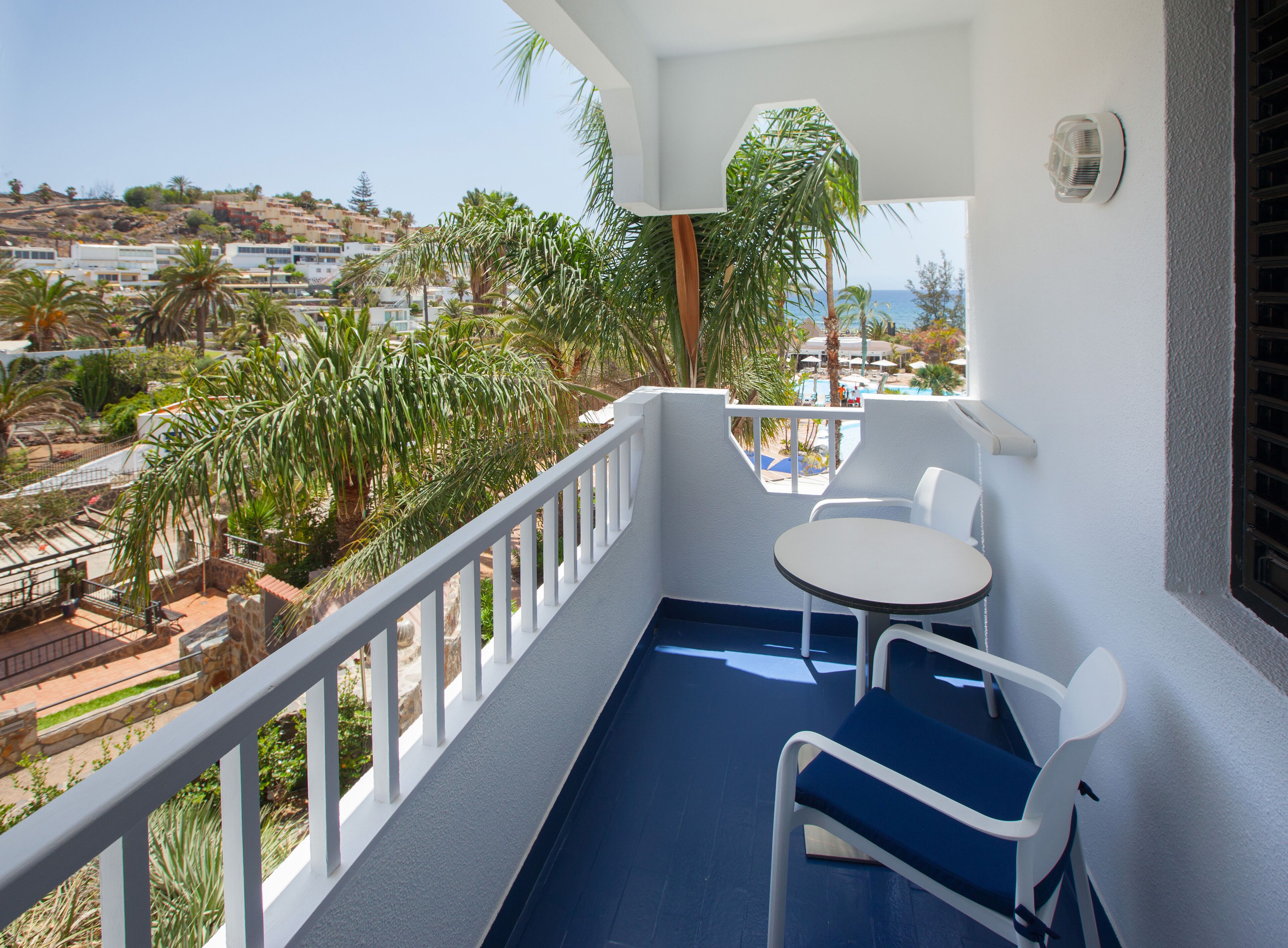 A balcony with a table and chairs, overlooking a pool and a coastal view.