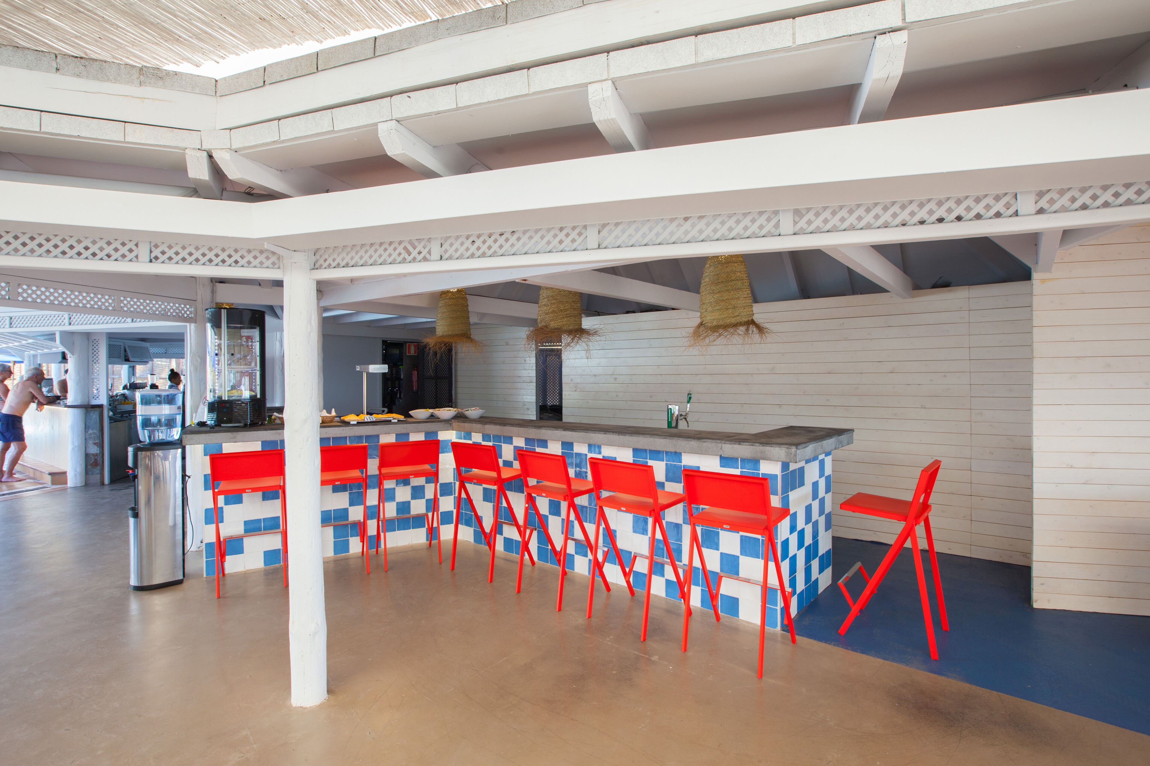 A spacious indoor area with a bar area featuring red chairs and a checkered tile design.