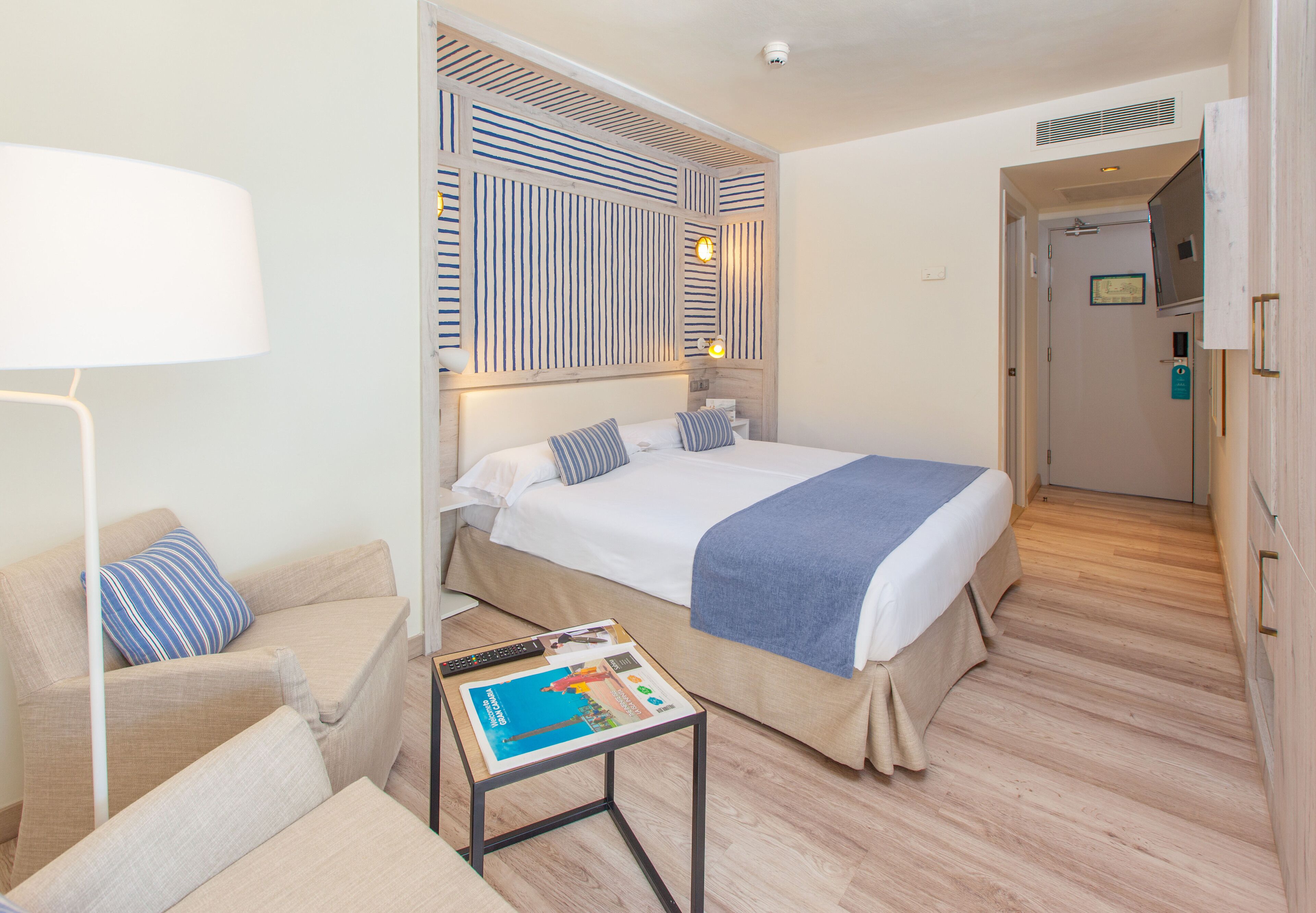 A hotel room with a bed, a sofa, a small table with a magazine, and a decorative wall panel.
