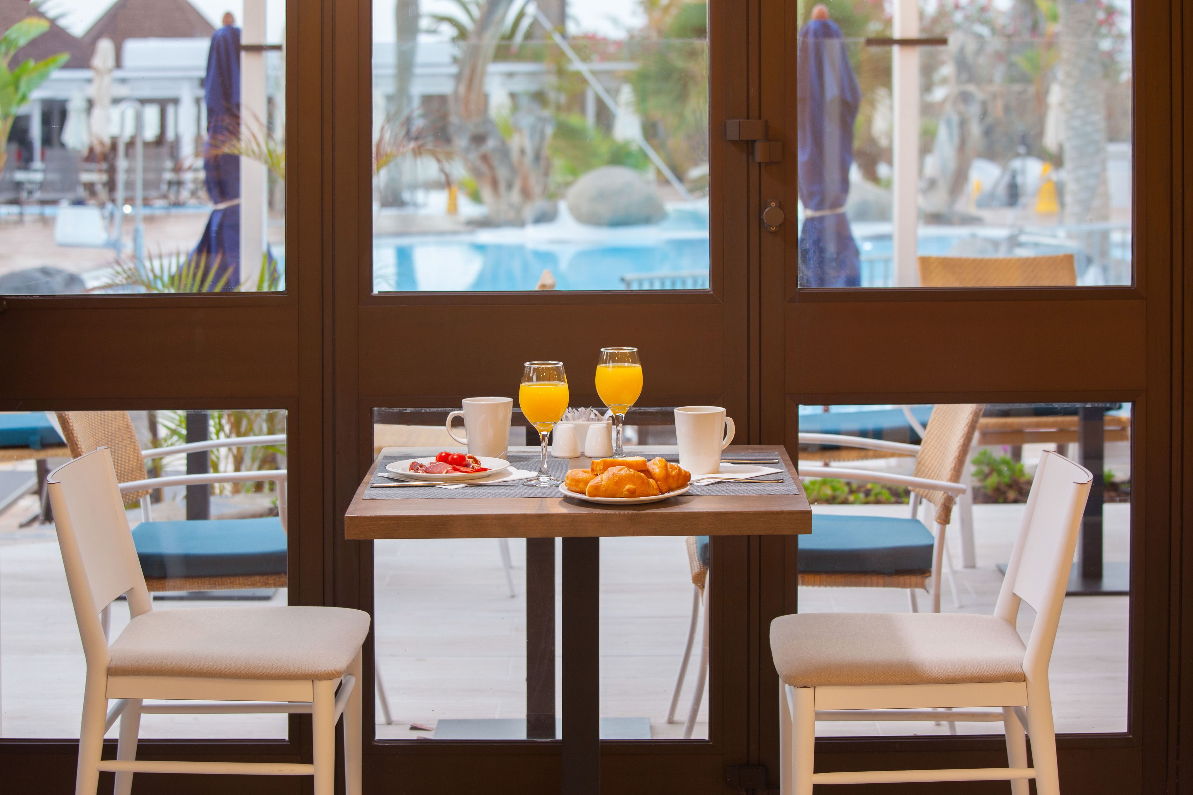 A breakfast table with two glasses of orange juice, a plate of croissants, and a cup of coffee.