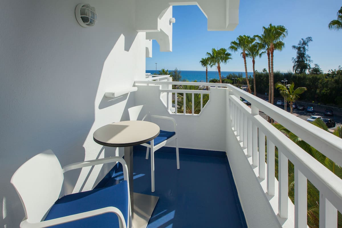 A balcony with a white railing, a small round table, and a blue chair.