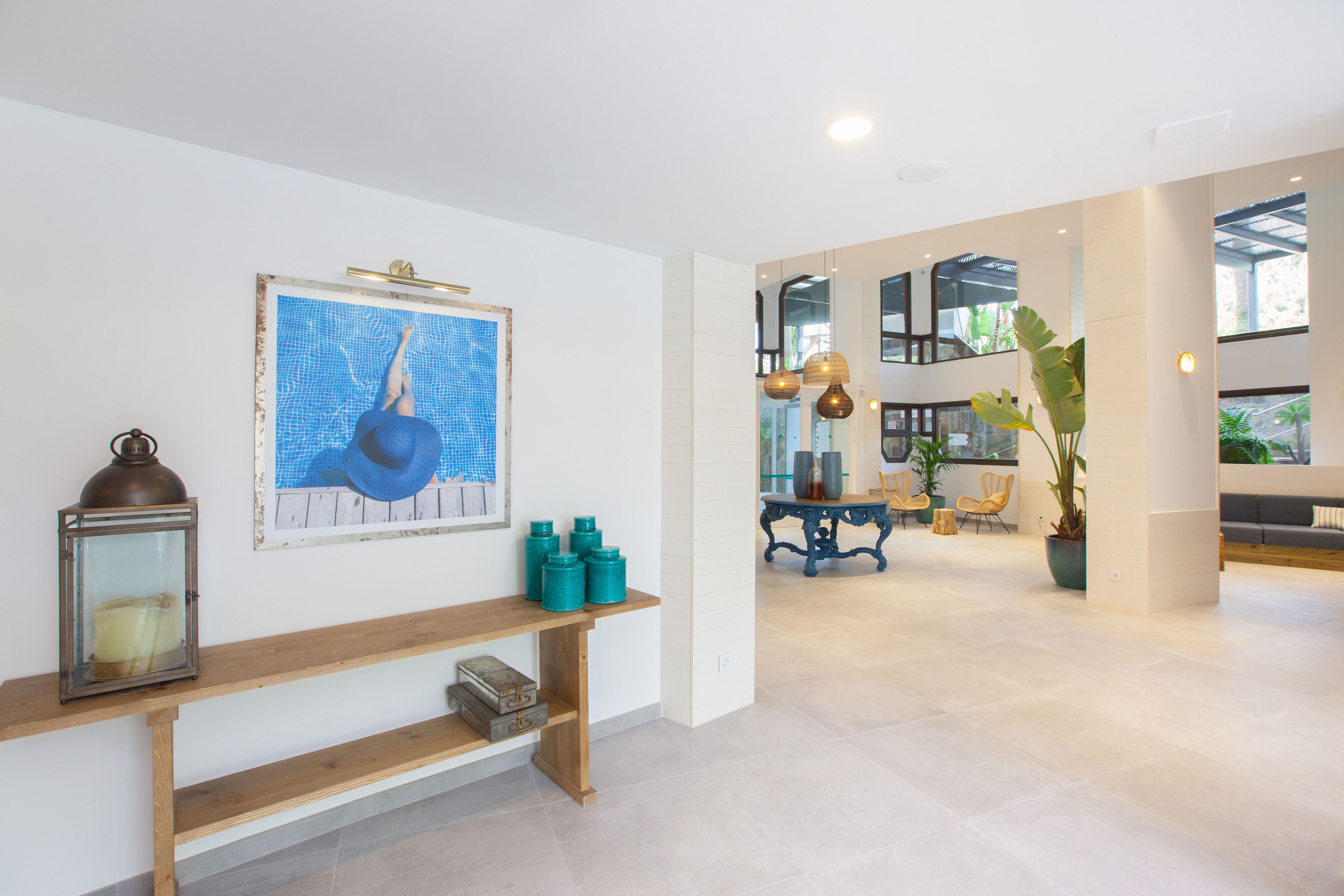 Un hall d’entrée spacieux, avec un banc en bois, une œuvre d’art encadrée, des récipients de couleur turquoise et une grande plante en pot.