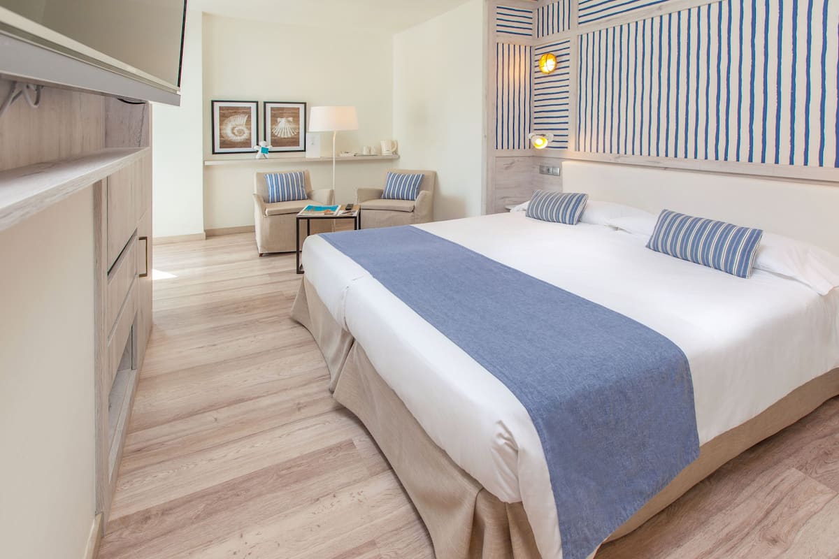 A hotel room with a large bed, a sofa, a desk, and a TV.
