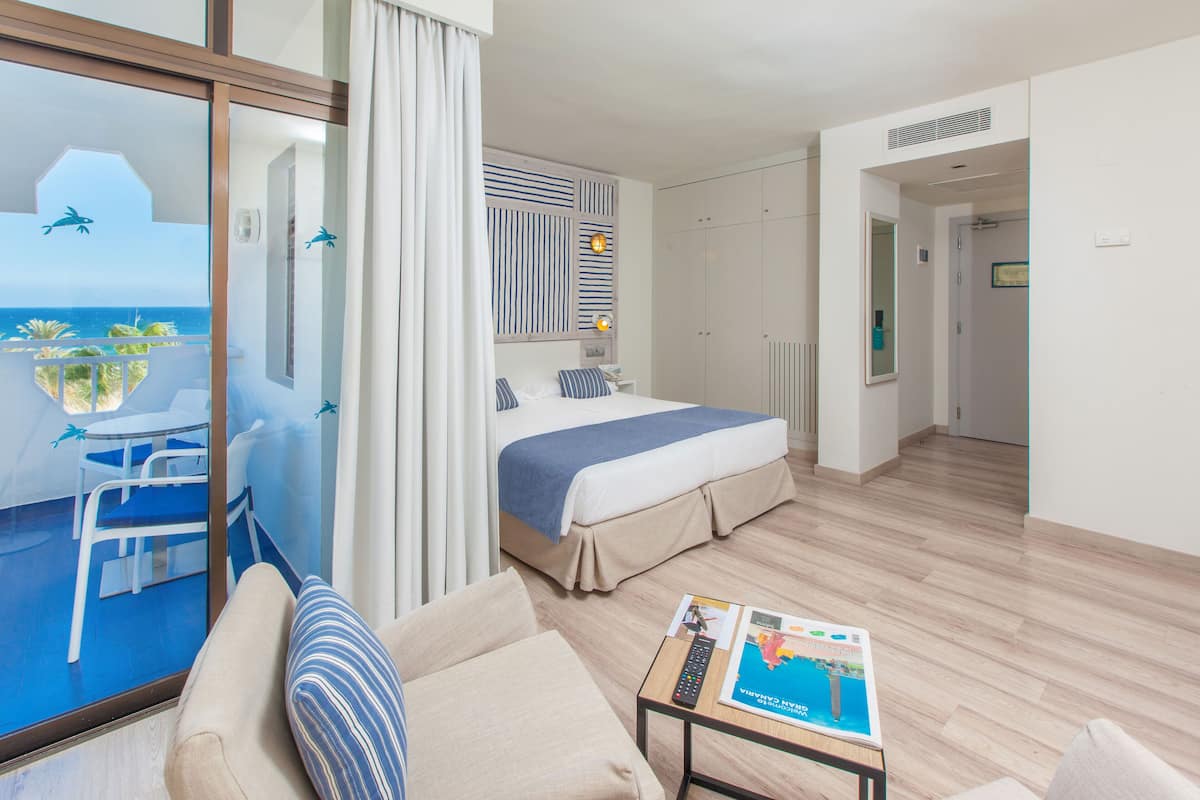 A hotel room with a balcony, a bed, a sofa, and a coffee table.