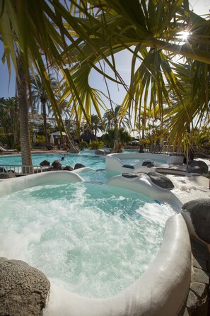 Un área de piscina con varias toboganes acuáticos, rodeada de palmeras y rocas.