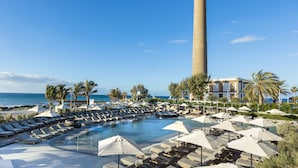 Zona de piscina con tumbonas y sombrillas, una torre alta y vista al océano.