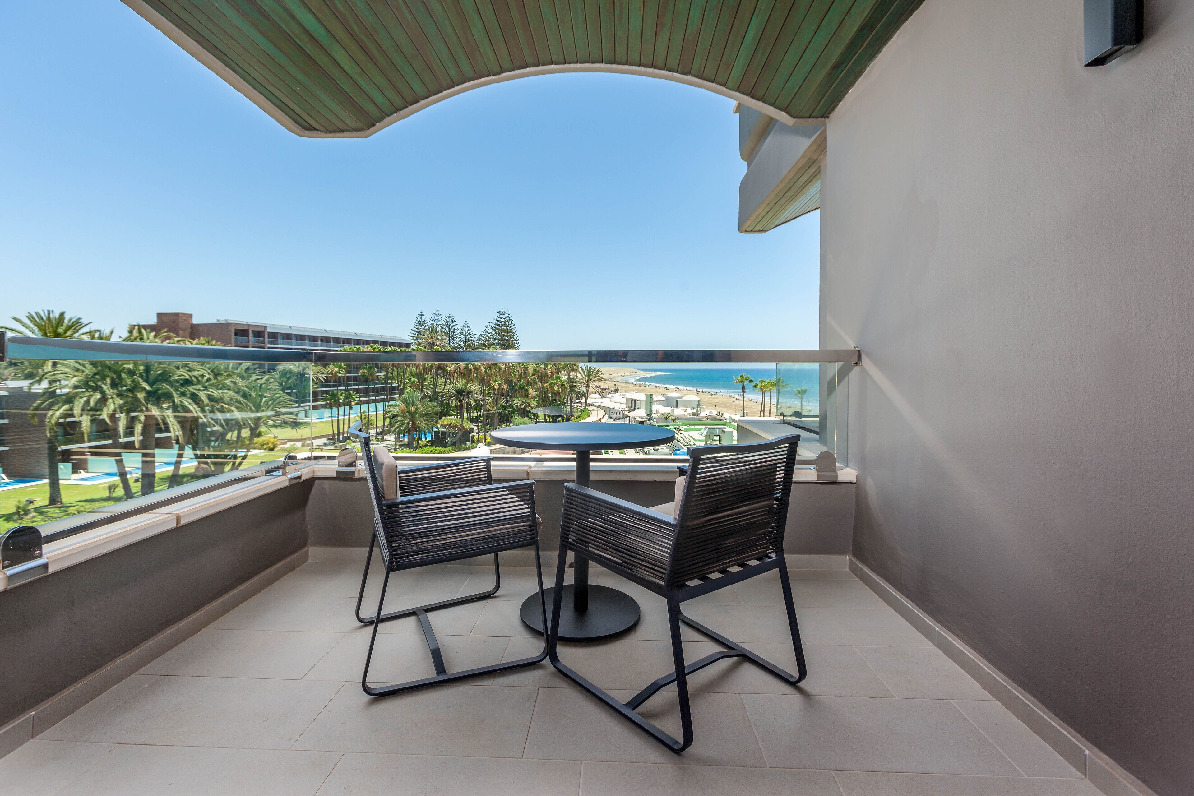 Un balcón con mesa y sillas, con vista a una playa y una piscina.