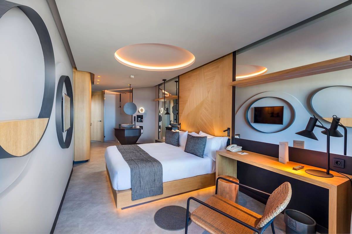 A modern hotel room with a large bed, a desk with a computer, and a chair.