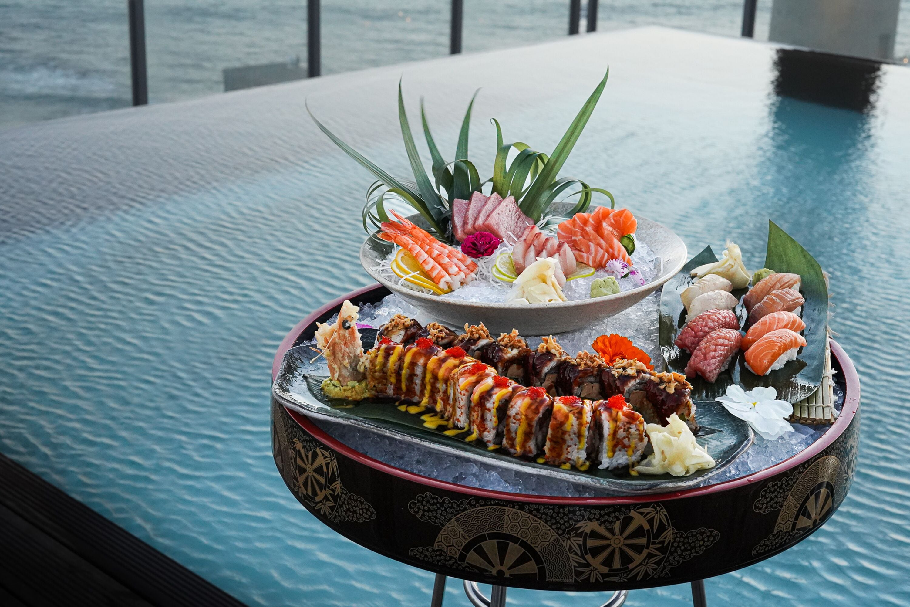 Una bandeja de mariscos con diferentes tipos de sushi y sashimi sobre una mesa redonda junto a una piscina.