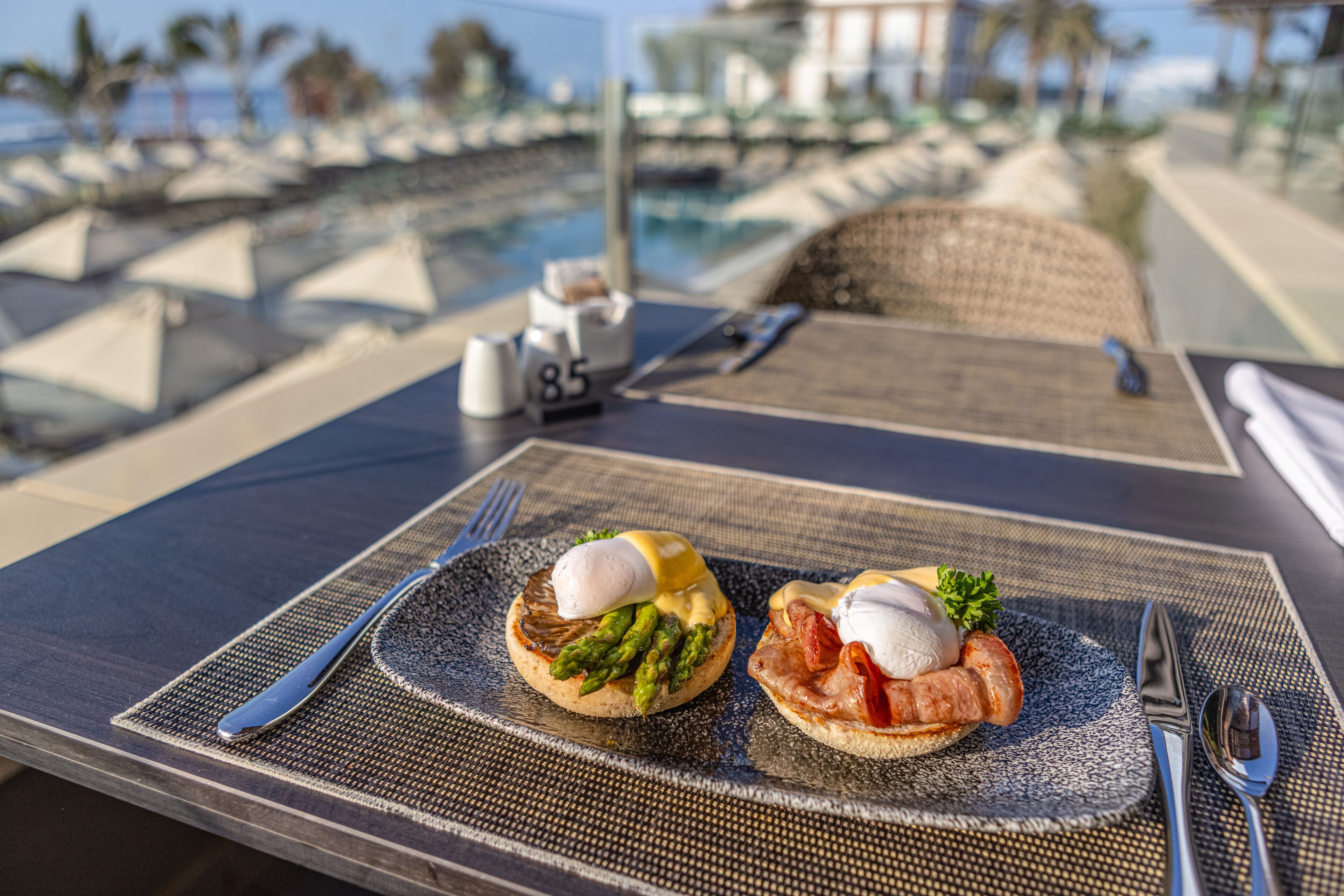 Un desayuno con dos platos de huevos benedictinos sobre una mesa, un tenedor, un cuchillo y una cuchara.