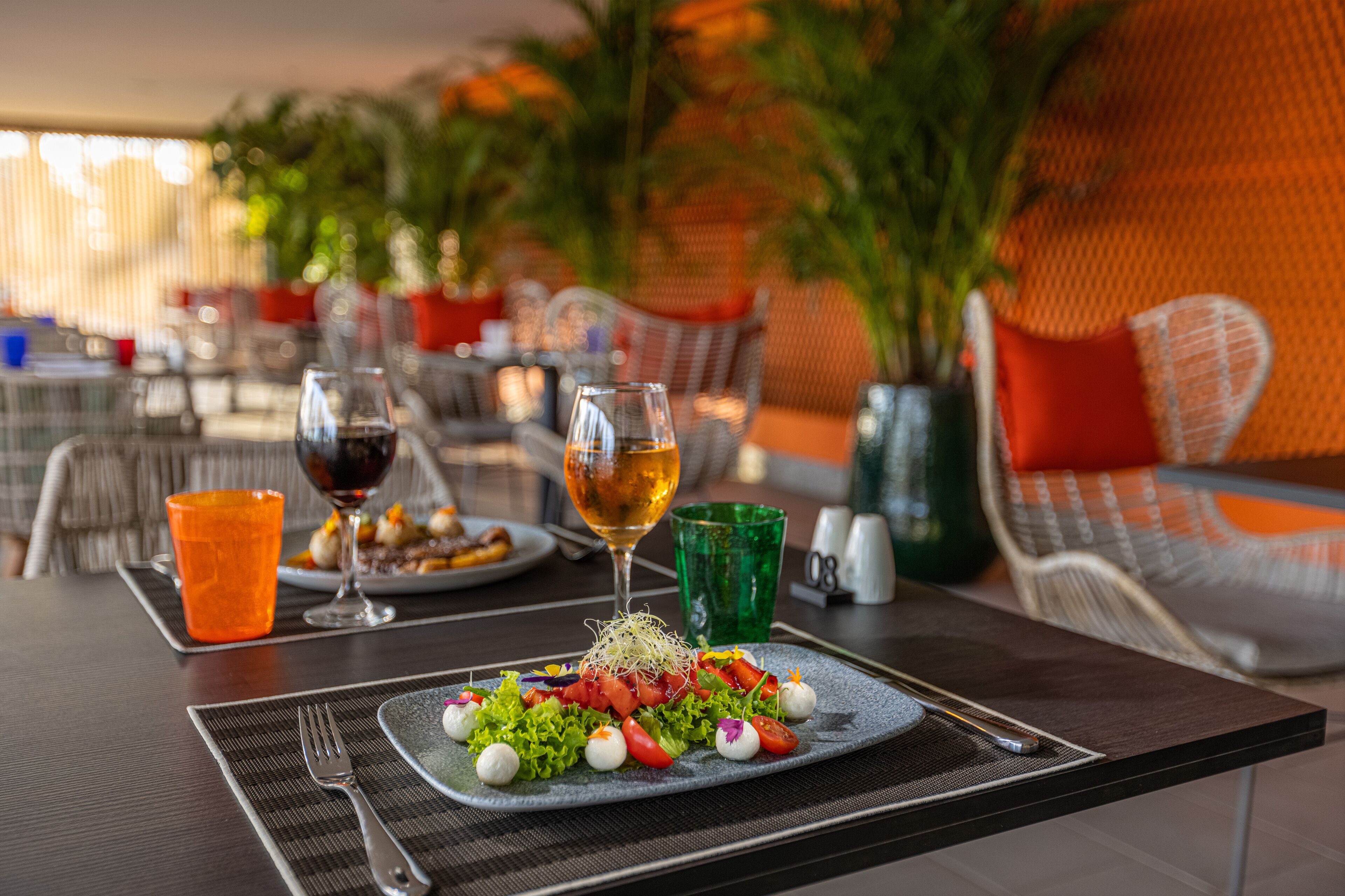 Una mesa de comedor con un plato de ensalada, dos copas de vino y un vaso verde.