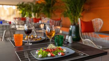Una mesa de comedor con un plato de ensalada, dos copas de vino y un vaso verde.